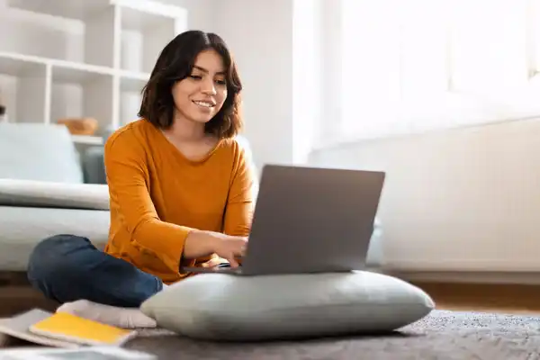 Mujer decide estudiar psicologia sentada en la alfombra de la sala frente a laptop