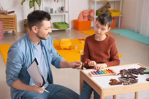 Egresado de la maestría en psicología clínica en sesión terapéutica con niño con recursos didácticos en un consultorio colorido con juguetes